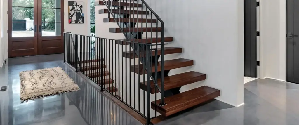 Modern Bay Area home entryway with gloss-sealed concrete microtopping floor, floating wood staircase, black metal railing, and French doors — Duraamen soundproof concrete flooring system